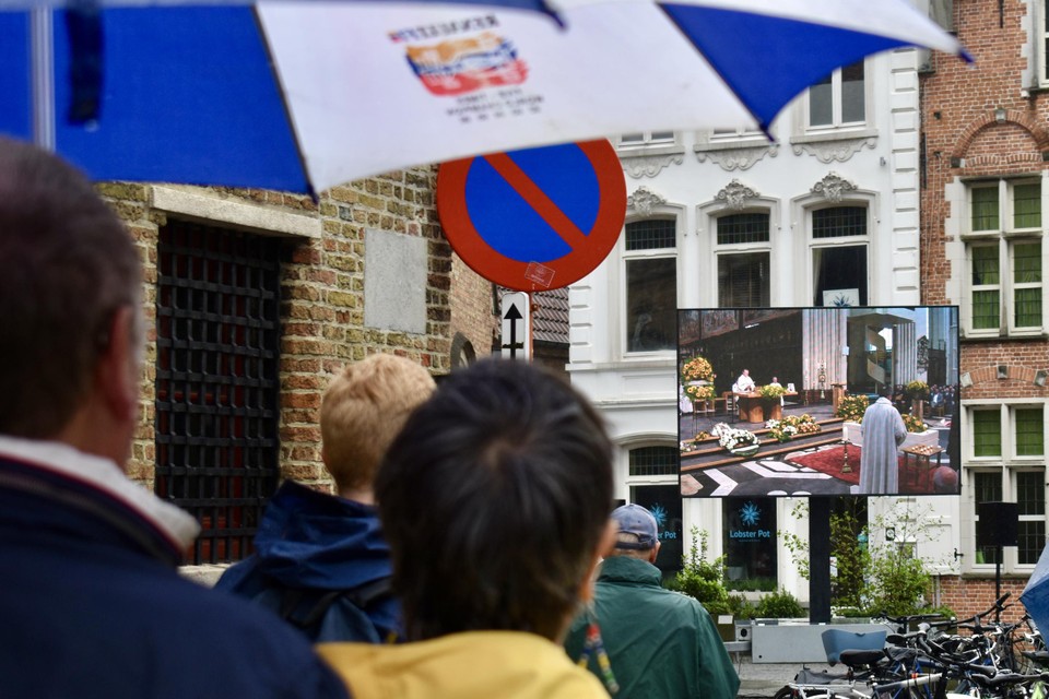 Terwijl het miezert, volgen ook buiten enkele tientallen Bruggelingen de plechtigheid op groot scherm.