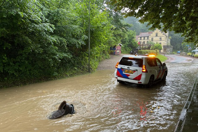 Een ondergelopen straat met putdeksel in Geulhem.